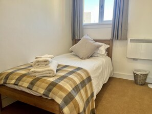 A neatly made bed with a plaid bedspread, a stack of folded towels, and a single pillow. - 2 Bed in Glentrool, Newton Stewart (oc-d616822) (Glentrool)
