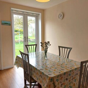 Un comedor con una mesa cubierta por un mantel estampado, rodeado de sillas y un reloj en la pared.