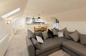 A modern living room with a sectional sofa, a dining area with a table and chairs, and a kitchen in the background. - 2 Bed in New Galloway (oc-d550751) (New Galloway)