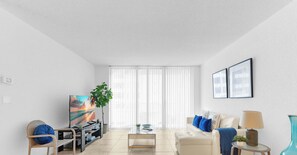 A modern living room with a flat-screen TV, a coffee table, a sofa, and a plant. - Stylish Comfort Elegant APT - Fully Equipped (Hollywood)