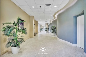 A hotel corridor with a polished floor, potted plants, and a modern ceiling design. - Stylish Comfort Elegant APT - Fully Equipped (Hollywood)