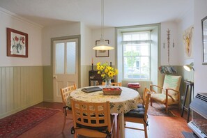 A dining area with a round table, chairs, a vase of yellow flowers, and a bookshelf. - 2 Bed in Kirkcudbright (oc-d546369) (Kirkcudbright)