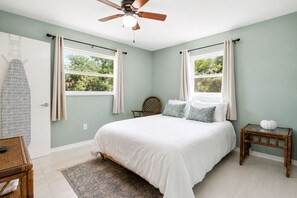 Una camera da letto con un letto, due finestre, una ventola a soffitto, un comodino e una sedia.