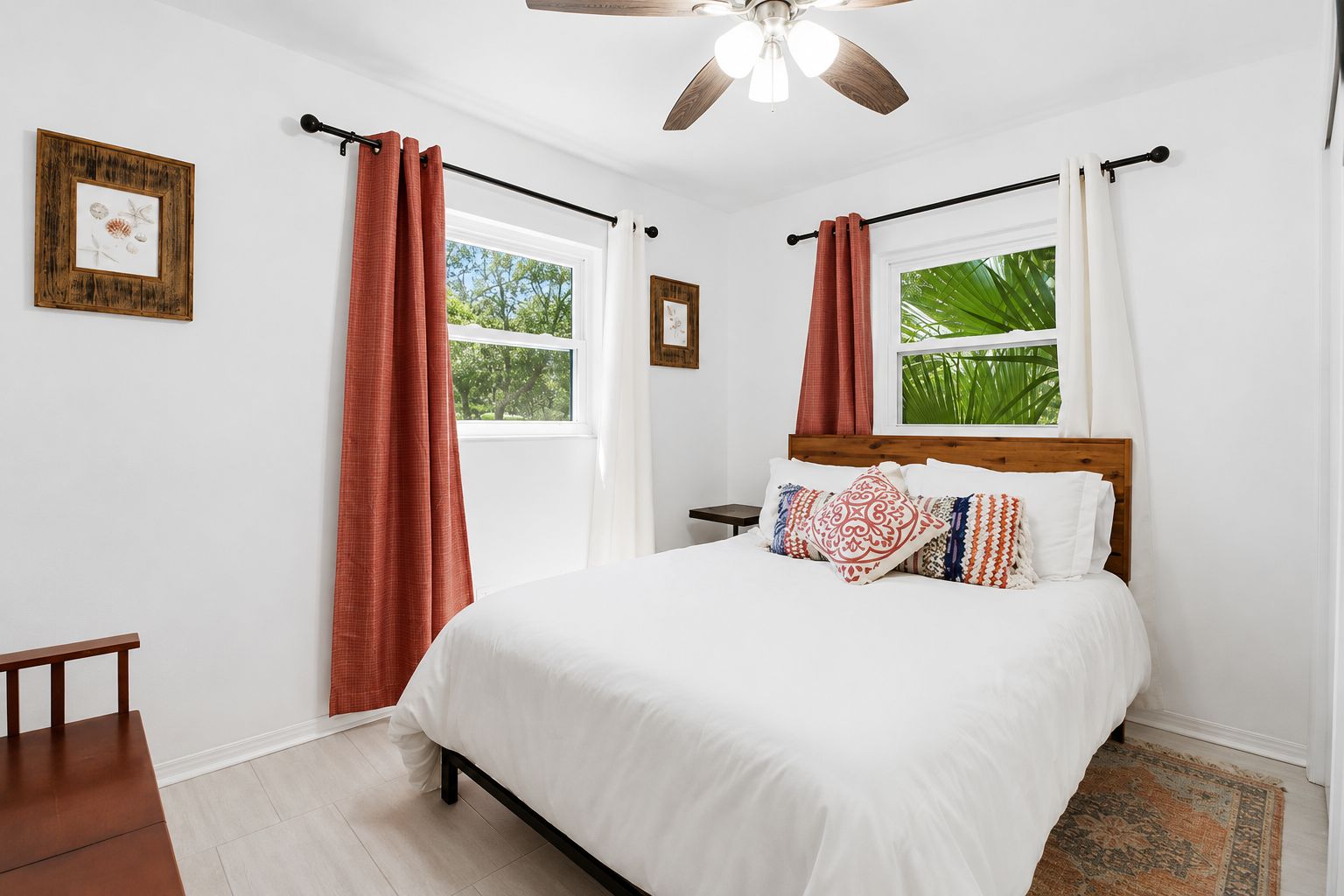 A bedroom with a bed, curtains, a ceiling fan, and a window with a view of greenery.