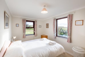 Ein Schlafzimmer mit einem großen Bett, zwei Vorhängen, einer Heizung, einem Nachttisch mit Lampe und Blick auf die Landschaft.