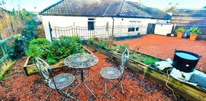 A house with a fenced backyard, a garden with various plants, and a metal table with chairs. - 2 Bed in Kirkcudbright (oc-d634817) (Kirkcudbright)