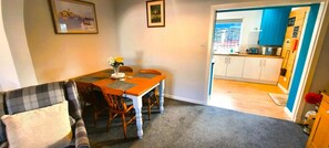 A dining area with a table, chairs, and a vase of flowers. There is a sofa with a cushion and a framed picture on the wall. - 2 Bed in Kirkcudbright (oc-d634817) (Kirkcudbright)