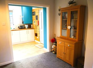 A kitchen with white cabinets, a microwave, and a toaster. There is a wooden cabinet with glass doors and a vase with flowers. - 2 Bed in Kirkcudbright (oc-d634817) (Kirkcudbright)