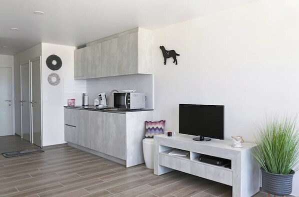 Una sala de estar moderna con una televisión de pantalla plana, una zona de cocina con microondas y un comedor con mesa y sillas.