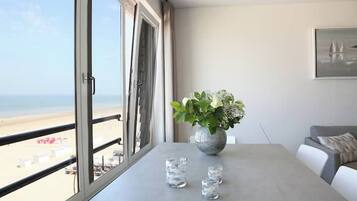 Une pièce dotée d’une grande fenêtre donnant sur une plage, d’une table ornée d’un vase de fleurs et d’un canapé.