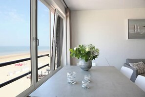 Una habitación con un ventanal que da a una playa, una mesa con un jarrón de flores y un sofá.