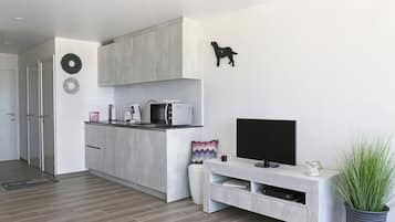 A modern living room with a flat-screen TV, a kitchen area with a microwave, and a dining area with a table and chairs.
