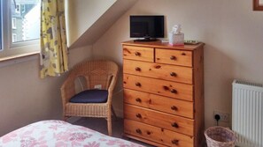 Ein Schlafzimmer mit einem Bett, einem hölzernen Schminktisch, einem Fernseher und einem Korbstuhl.
