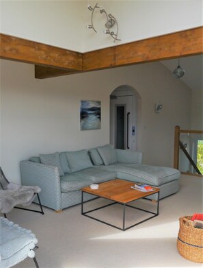 Ein Wohnzimmer mit einem Ecksofa, einem Holztisch, einem Gemälde und einer Treppe.