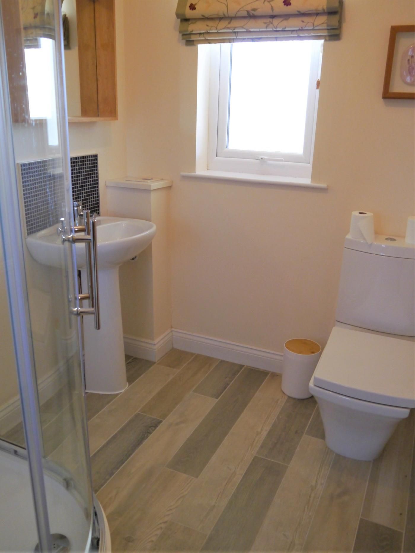A bathroom with a glass shower enclosure, a sink, a toilet, and a window.