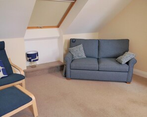 Ein Zimmer mit grauem Sofa, blauem Sessel, einer Lampe und einem Oberlicht.