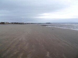 A wide sandy beach with a calm sea, distant buildings, and overcast sky. - 2 Bed in Prestwick, Ayr (oc-d545675) (Prestwick)