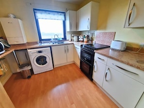 A compact kitchen with a washing machine, oven, and a toaster. - 2 Bed in Prestwick, Ayr (oc-d545675) (Prestwick)
