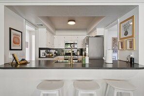 Cook up a feast in this open kitchen with bar seating, sleek countertops, and stainless appliances ready for any meal. - Southbound Social | Pool • Patio • Games & Movies (Austin)