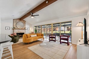 Gather around the stone fireplace in this warm living room, with vaulted ceilings and sliding doors opening out to the yard. - Southbound Social | Pool • Patio • Games & Movies (Austin)