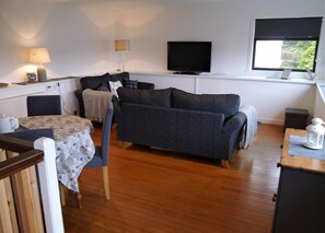 A cozy living room with a sofa, a table with chairs, a television, and a window with a view. - 2 Bed in Kippford (oc-d564011) (Kippford)