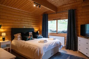 Ein Schlafzimmer einer Holzhütte mit Bett, Nachttischlampe und Fernseher.