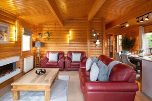 Ein Blockhaus-Interieur mit Kamin, Ledersofas, einem Esstisch und Blick ins Freie.