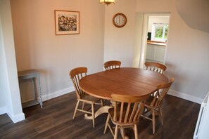 A dining room with a round wooden table and six chairs, a small side table, a clock, and a framed picture on the wall. - 4 Bed in Rockcliffe (oc-d585846) (Rockcliffe)