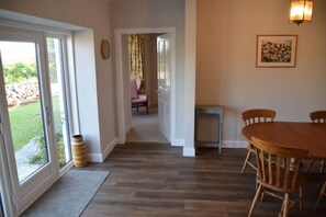 A hallway leading to a dining area with a table and chairs, a small side table, and a door with a curtain. - 4 Bed in Rockcliffe (oc-d585846) (Rockcliffe)