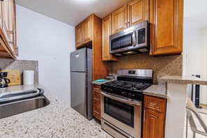 A compact kitchen with wooden cabinets, a stainless steel refrigerator, a microwave, a gas stove, and a built-in oven. - Amazing Berryman # 8 (Los Angeles)