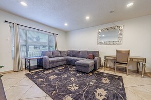 A living room with a sectional sofa, a small table, a chair, a decorative mirror, and a patterned rug. - Amazing Berryman # 8 (Los Angeles)