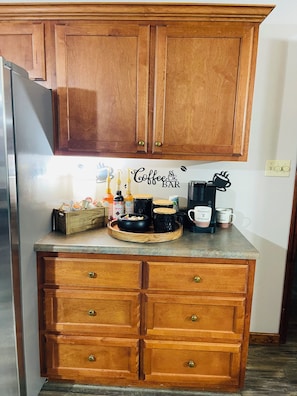 A kitchen with wooden cabinets, a countertop with coffee-making equipment, and a sign that reads 'Coffee Bar'.