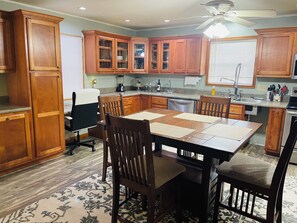 A kitchen with wooden cabinets, a dining table with chairs, a ceiling fan, and a window with blinds.