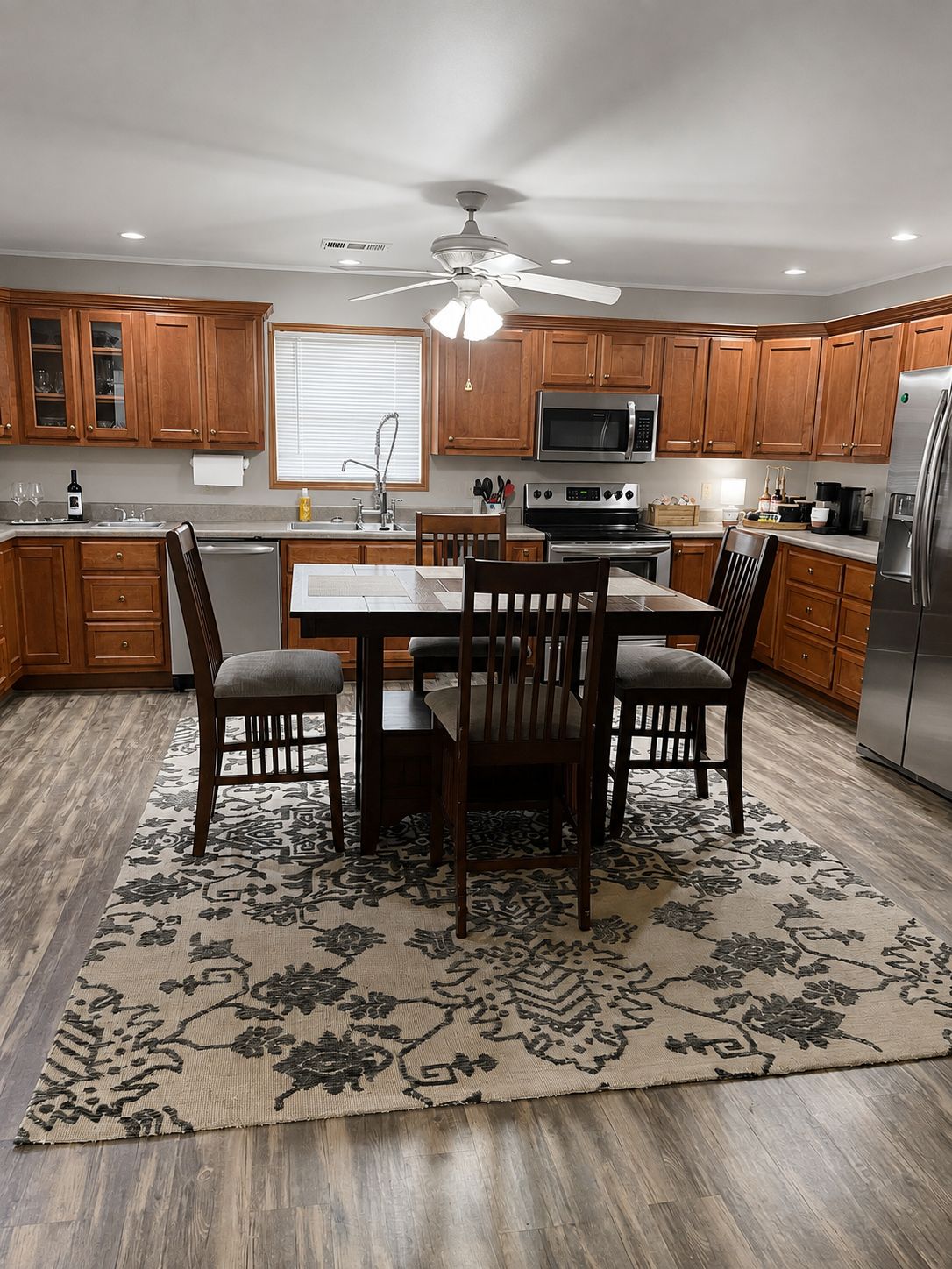 A kitchen with wooden cabinets, a dining table with chairs, a ceiling fan, and a refrigerator.