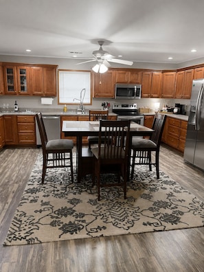 A kitchen with wooden cabinets, a dining table with chairs, a ceiling fan, and a refrigerator.