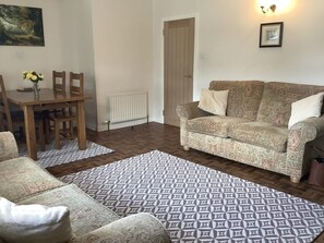 A living room with a sofa, a dining table with chairs, a patterned rug, and a radiator. - 2 Bed in Lochcarron (oc-d546536) (Lochcarron)