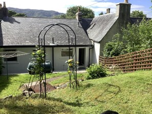 A house with a sloped roof, a garden with a wooden fence, and a clothes drying frame. - 2 Bed in Lochcarron (oc-d546536) (Lochcarron)