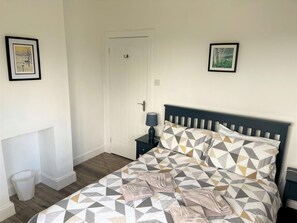 A bedroom with a bed, a nightstand, a door, and two framed pictures on the walls. - 3 Bed in Rockcliffe (oc-d546117) (Rockcliffe)