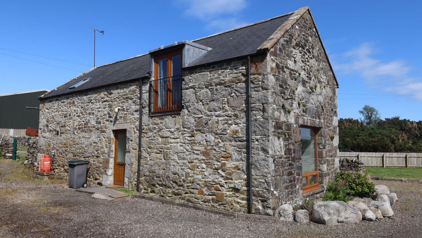 A stone building with a sloped roof, a wooden door, and a window with a black frame.