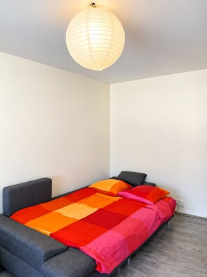 Ein Einzelbett mit farbenfroher Decke, einem grauen Kopfteil und einer hängenden Lampenleuchte.