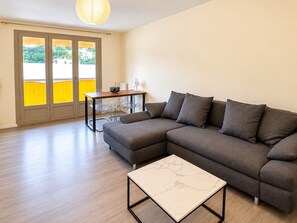 Ein modernes Wohnzimmer mit einer Eckcouch, einem kleinen Tisch und Blick durch eine Glastür.