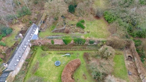 Eine Vogelperspektive zeigt ein Anwesen mit einem langen, schmalen Gebäude, einem kreisförmigen Garten und einem kleinen Spielplatz.