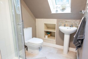 Un bagno con box doccia in vetro, un water, un lavandino e un piccolo oblò sopra il lavandino.