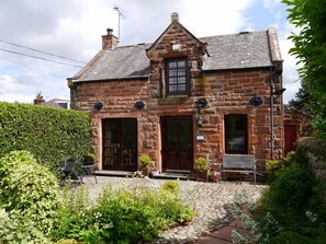 A stone house with a traditional design, featuring a front door, two windows, and a small porch area with potted plants. - 2 Bed in Dumfries (oc-d589143) (Dumfries)