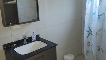A bathroom with a white sink, dark cabinetry, a mirror, and a shower curtain with a sea shell pattern.