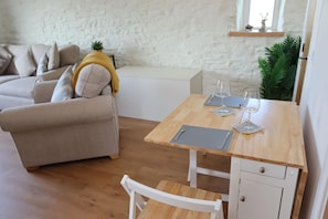 Ein gemütlicher Wohnbereich mit einer Couch, einem Esstisch mit Weingläsern und einer kleinen Pflanze.
