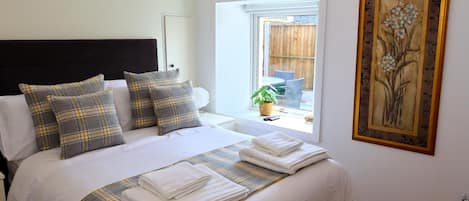 A neatly made bed with plaid bedding, a window with a view of outdoor furniture, and a framed floral artwork on the wall.