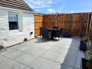 Eine Terrasse mit Tisch und Stühlen, ein Holzzaun und ein weißes Gebäude.