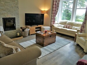 A living room with a fireplace, television, sofa, and a wooden chest. - 4 Bed in Castle Douglas (oc-d615180) (Corsock)