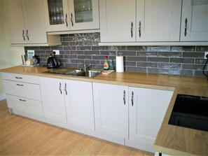 Una cocina moderna con armarios blancos, un lavamanos de acero inoxidable y un salpicadero de azulejos negros.